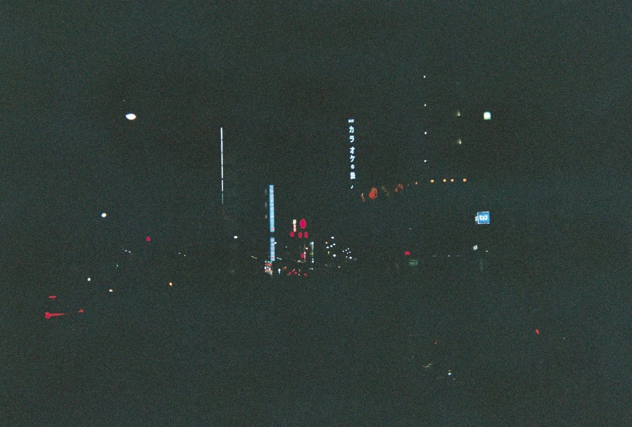 夜の街のフィルム写真。フラッシュを焚いていないため小さな街灯や看板の光しか映っていない。
